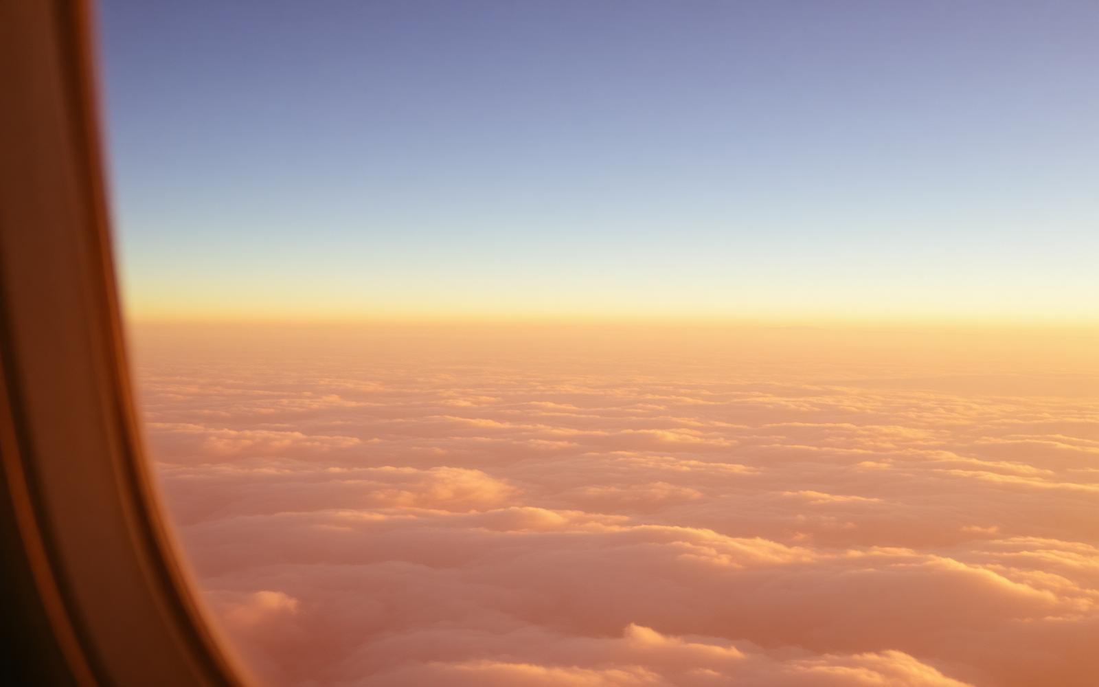 Vista da janela do avião sobre nuvens ao pôr do sol